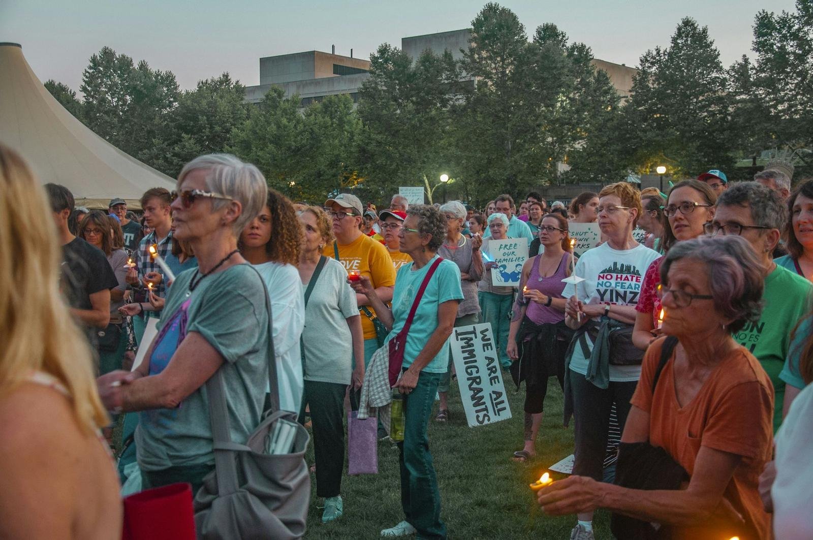 People at an evening vigil holding candles and signs