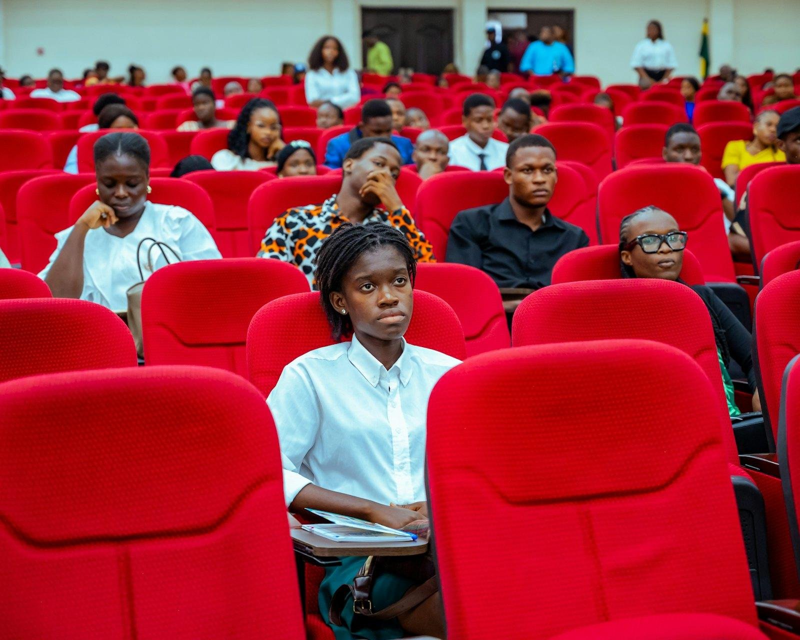 Audience members seated in a red-seated auditorium
